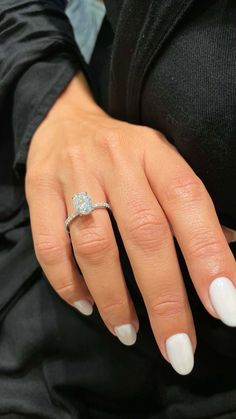 a woman's hand with a diamond ring on her left hand and white nails