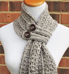 a white mannequin wearing a gray crochet scarf with buttons on it