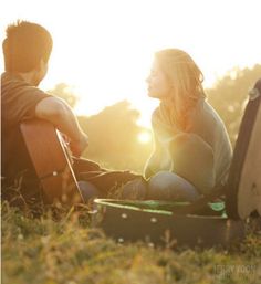 two people sitting in the grass with their guitars