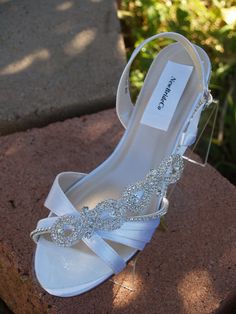 a pair of white wedding shoes sitting on top of a brick wall next to bushes