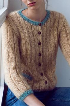 a woman sitting on the window sill wearing a knitted sweater and blue jeans