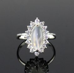 This Sterling Silver Ring features an Elegant Art With Natural Moonstone Gemstone. The cavity is made from genuine solid 925 sterling silver and stamped as S925. This Jewelry is Lead free and Rhodium Plated to keep polish long time and Scratches free. ITEM DESCRIPTION Item Code: JARG337/12 Metal: 925/92.5 Sterling Silver Gemstone: Genuine Natural Moonstone Cabochon Gemstone Shape: Marquise Gemstone Size: 6 X 12 MM Ring Length: 18 MM Ring width: 11 MM Second Stone: Cubic Zirconia Weight: 3.2 gm a Fine Jewelry Silver Hallmarked Moonstone Ring, Silver Moonstone Ring With Halo Setting For Wedding, Silver Moonstone Ring With Accent Stones, Silver Moonstone Promise Ring With Accent Stones, Silver Crystal Halo Ring As Gift, Silver Moonstone Ring For Formal Occasions, Silver Sterling Moonstone Wedding Ring, Elegant Silver Moonstone Ring With Stone Setting, Formal Silver Moonstone Ring With Center Stone