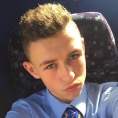 a young boy wearing a blue shirt and tie sitting in a chair looking at the camera