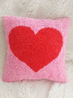 a pink and red pillow with a heart on the front, sitting on a white furnishing