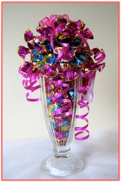 a glass vase filled with lots of purple and gold confetti on top of a white table