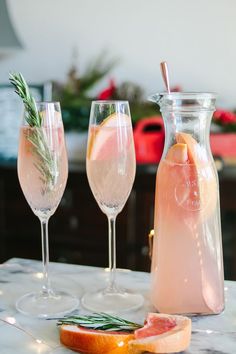 three wine glasses and a pitcher sitting on a table next to grapefruits