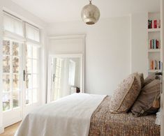 a bedroom with white walls and flooring has a bed in the middle, two windows on both sides