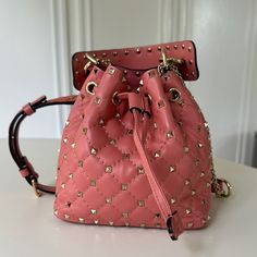 Crafted In Italy From Rose Pink Leather, This Valentino Garavani Bucket Bag Spotlights A Single Top Handle That's Embellished With Signature Rockstud Detailing Designer Pink Satchel Bucket Bag, Travel Pouch Bag With Branded Hardware, Branded Hardware Pouch Satchel, Designer Satchel Bucket Bag With Branded Hardware, Designer Bucket Bag With Branded Hardware, Designer Satchel Bucket Bag, Bucket Bags With Branded Hardware For Shopping, Tote Shaped Bucket Bag For Errands, Bucket-shaped Backpack With Dust Bag Included