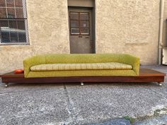 a green couch sitting on top of a wooden table in front of a building with a door