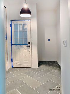 an empty room with white walls and blue tape on the door, and a black light hanging from the ceiling