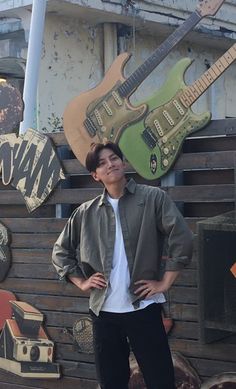 a young man standing in front of a wall with guitars on it's sides