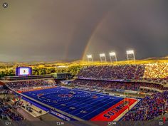 a football stadium filled with lots of people under a cloudy sky and a rainbow in the distance