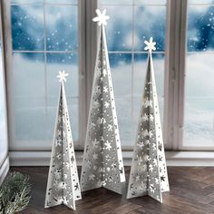 three white christmas trees sitting on top of a wooden floor next to an open window