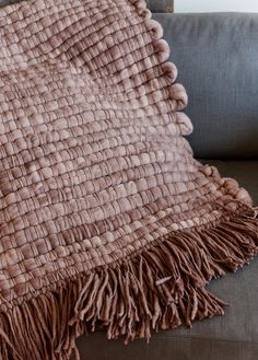 a brown blanket sitting on top of a couch next to a gray sofa cushion with tassels