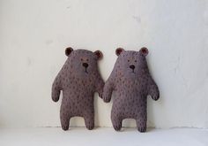 two stuffed bears are sitting next to each other on a white surface, one is brown and the other is gray