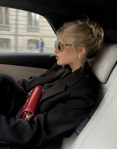 a woman sitting in the back seat of a car with her arm wrapped around a red purse