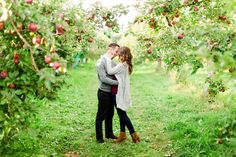 two people standing in an apple orchard holding each other