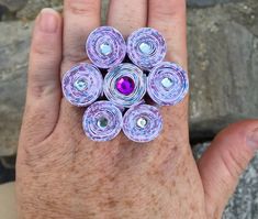 a person's hand holding a ring made out of rolled up paper and gems