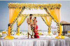 a newly married couple standing in front of an outdoor ceremony setup with yellow draping and flowers