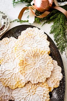 some cookies are on a black plate and decorated with greenery next to a pink ornament