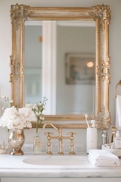 a bathroom sink with a gold framed mirror above it and flowers on the counter top