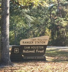 a sign for the sam houston ranger station in front of some trees and leaves on the ground