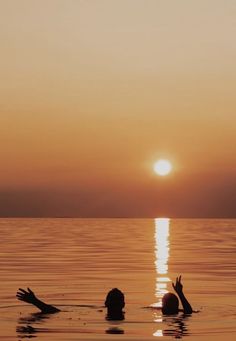 two people floating in the water at sunset with their hands up to the sun above them