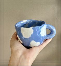 a hand holding a blue and white cup with clouds painted on the inside of it