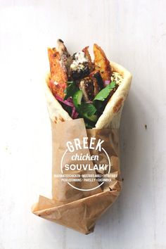 a wrapper filled with meat and vegetables on top of a white table next to a brown paper bag