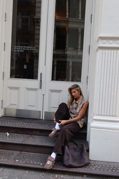 a woman sitting on the steps in front of a building with her feet propped up