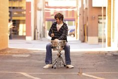 a man sitting on top of a drum set in the middle of an empty parking lot