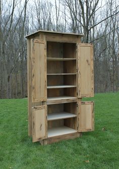 a large wooden cabinet sitting in the middle of a grass covered field next to trees