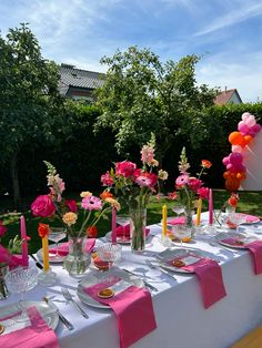 the table is set with pink and orange flowers, candles, plates and napkins