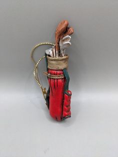 a red vase with some silver items in it on a white table and gray background