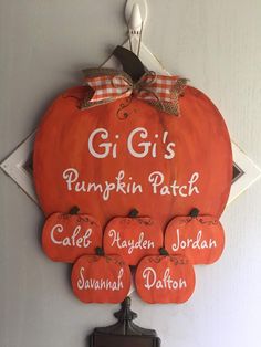 an orange pumpkin hanging on the wall with names written in white and black, along with six smaller pumpkins