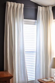 a bed sitting under a window next to a wooden table with a lamp on top of it