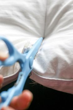 a person holding a pair of blue scissors in front of a pillow on the floor