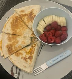 a plate with fruit and quesadilla on it next to a bowl of raspberries