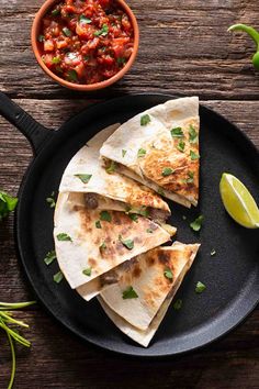 quesadillas on a black plate with salsa and limes next to it