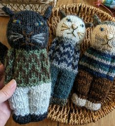 three knitted cats in sweaters are sitting on a basket next to a person's hand