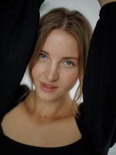 a woman with blue eyes and black sweater posing for the camera while holding her hands behind her head