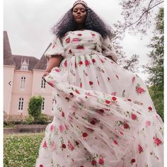 a woman in a white dress with flowers on it is standing near a pink house