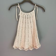 a white crochet top hanging on a hanger against a gray wall,