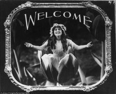 a black and white photo of a woman with her arms outstretched in front of a welcome sign