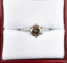 a ring with a brown diamond on it in a red velvet presentation box that has white fur lining around the edges