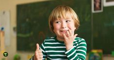 a young boy in a green and white striped shirt giving the thumbs up