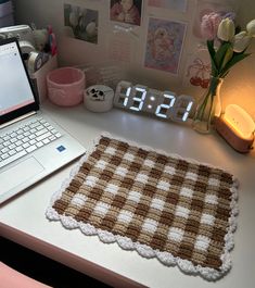 a laptop computer sitting on top of a desk next to a clock and flower vase