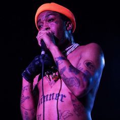 a man with tattoos on his chest holding a microphone and wearing an orange beanie