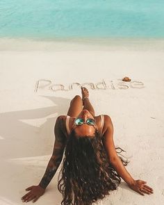 a woman laying on top of a sandy beach next to the word paradise written in sand