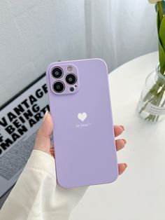 a person holding a purple iphone case with a heart on the back in front of a white table